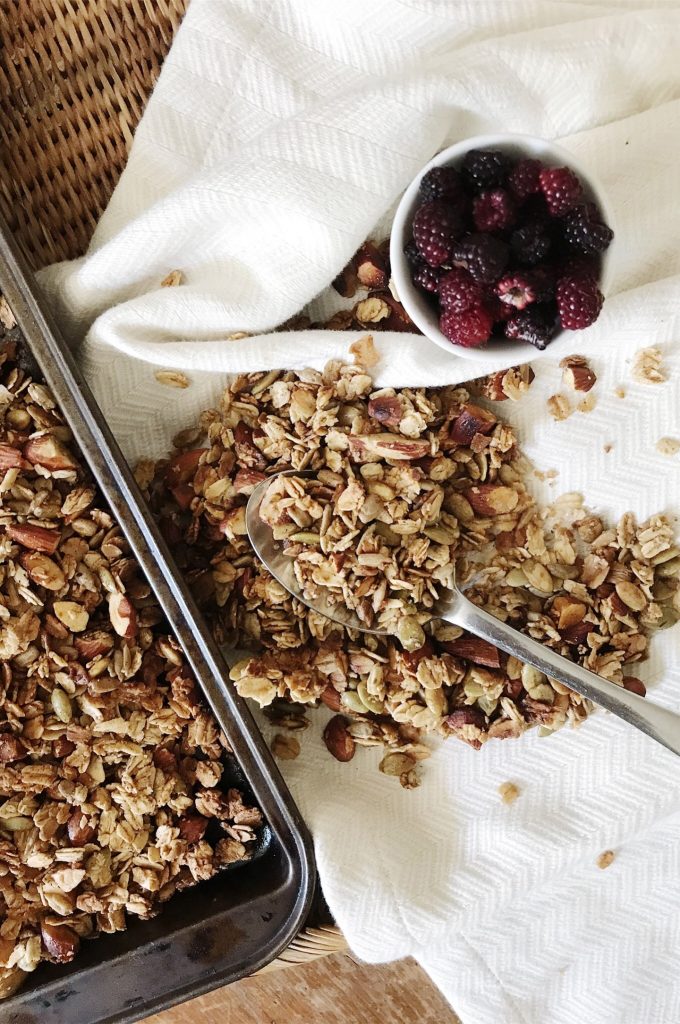 gluten-free homemade granola spilled out on tea towel with spoon and a small bowl of raspberries