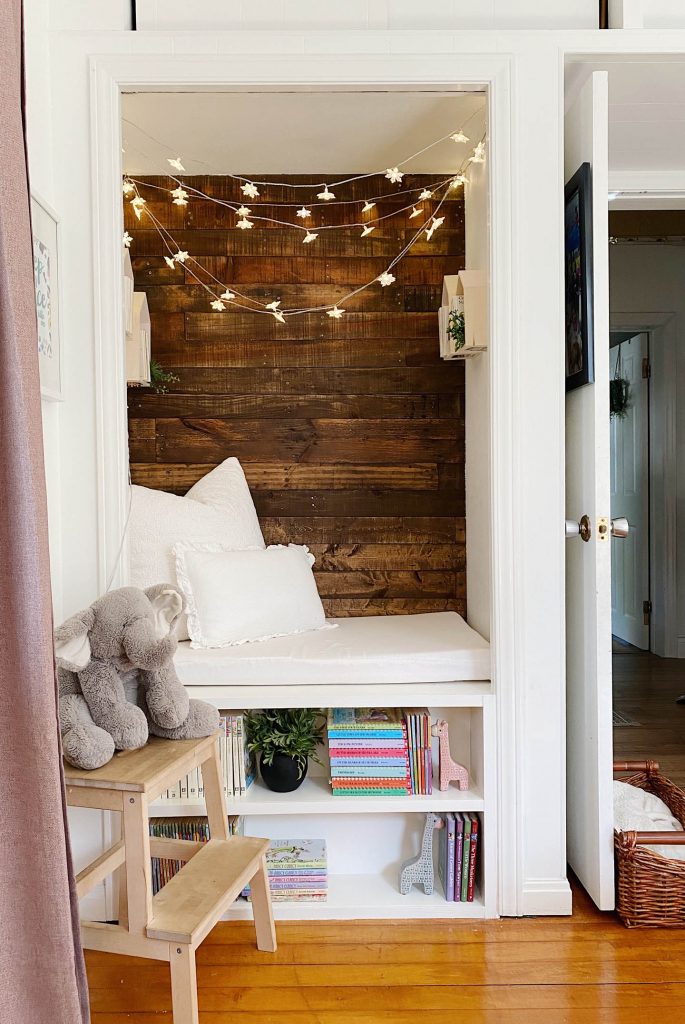 diy reading nook with stained wooden back, lights hanging above and builtin bookshelf below 